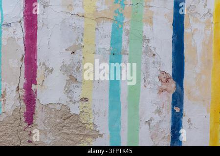 Handgemalte vertikale Regenbogenstreifen in Magenta, Türkis, Mintgrün, Blau und Gelb auf einer rissigen, abblätternden weißen Putzwand Stockfoto