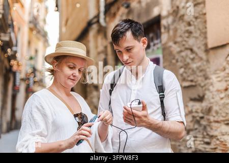 Zwei Reisende überprüfen ein Smartphone in einer engen Straße in Barcelona, umgeben von verwitterten historischen Gebäuden. Stockfoto