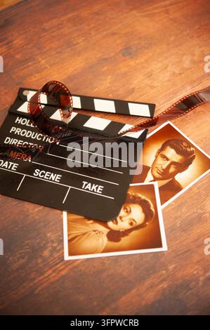 sepiatoniertes Kino-Stillleben mit einem Hollywood-Filmklappe, gekräuseltem Filmstreifen und zwei vintage-stil Porträtfotografien auf Holz Stockfoto