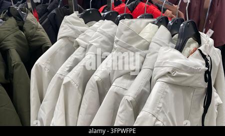 Weiße Winterjacken mit Kapuze hängen an einem Kleiderständer in einem Secondhand-Laden Stockfoto