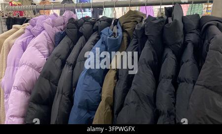 Bunte Winter-Pufferjacken, die an einem Kleiderständer in einem Secondhand-Laden hängen Stockfoto