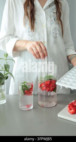 Vertikale Nahaufnahme von Glasbechern mit frischen Erdbeerscheiben, Minzblättern und Eiswürfeln auf einem hellen Hintergrund. Stockfoto