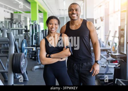 Glücklicher athletischer schwarzer Mann und Frau, die zusammen in einem hellen Fitnessstudio stehen Stockfoto