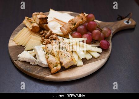 Käseplatte mit Trauben, Walnüssen und geröstetem Brot auf Holzbrett Stockfoto
