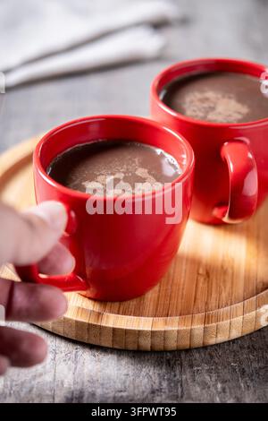 Heiße Schokolade in roter Keramiktasse auf Holztablett Stockfoto