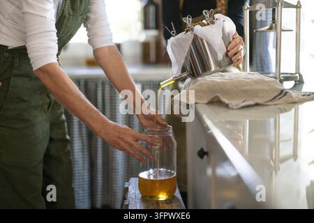 Frau filtriert frisch gepresstes Öl in ein großes Glasgefäß Stockfoto