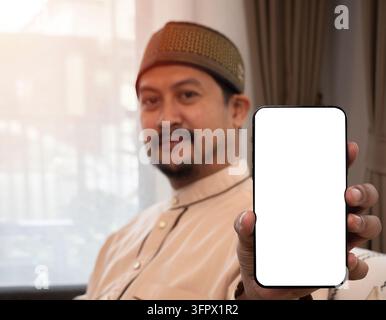 Nahaufnahme der Hand eines jungen asiatischen muslimischen Mannes, der ein Mobiltelefon hält, mit einem lächelnden Gesichtsausdruck. Isolierter Bildschirm auf Mobil-Mockup Stockfoto