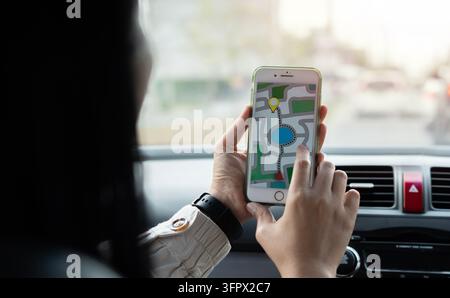 Rückansicht über die Schulter einer schwarzen Passagierin, die ein Handy hält und mit dem Finger auf den Bildschirm des Mobiltelefons zeigt, um es für einen Mock-up zu verwenden, während sie vor dem Meer sitzt Stockfoto