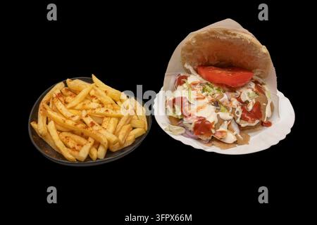 Döner Kebab in Pita-Brot mit Salat und Saucen, begleitet von einer Beilage aus paprikagewürzten Pommes frites. Stockfoto