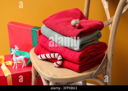 Weihnachtsvorbereitung und Feiereinkäufe, Stapel warmer Strickpullover auf einem Holzstuhl mit festlichen Ornamenten und verpackten Geschenken im Hintergrund Stockfoto