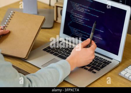 Softwareentwicklung und Programmierausbildung, Programmierer arbeitet an einem Laptop mit Quellcode und Notizbuch am Schreibtisch für das Erlernen der Informatik und Training Stockfoto