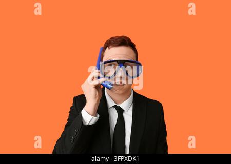 Arbeitsburnout und Stress, Geschäftsmann mit Schnorchelausrüstung und Anzug telefoniert im Büro, Humorkonzept auf orangefarbenem Hintergrund Stockfoto