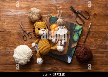 Handgemachte Amigurumi-Spielzeuge, kreatives Hobby und Bastelprojekt mit gehäkelten Löwen- und Hasenpuppen auf einem Holztisch mit Garnknäueln und Nähscheren Stockfoto