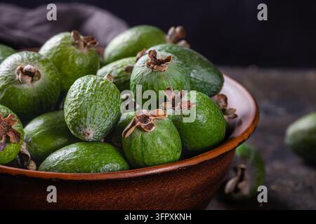 Augenhöhe-Studio-Lebensmittelfotografie einer rustikalen handgefertigten rötlich braunen Terrakotta-Tonschale, die mit frischen grünen Feijoa-Ananas-Guaven überläuft o Stockfoto