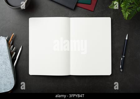 Oberansicht eines geöffneten schwarzen Hardcover-Notizbuchs mit Federtasche und Büromaterial auf dunklem Steinboden mit Kopierraum Stockfoto