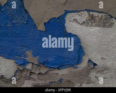 Eine detaillierte Nahaufnahme, die Abschnitte von lebhaftem blauem Lack zeigt, der von einer rauen Betonwand abblättert und sich ablöst. Die freigelegten Stellen zeigen eine Textur Stockfoto