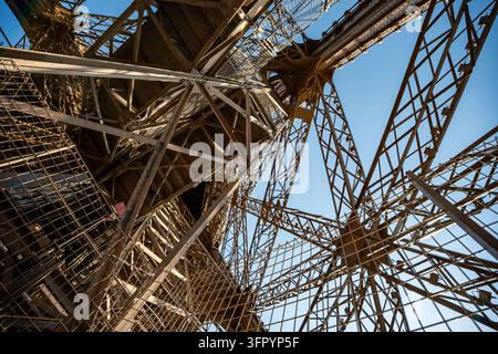 Detaillierte Niedrigwinkelansicht des kunstvollen Eisenlattgerüsts, der Balken und der Sicherheitsnetzstruktur des ikonischen Eiffelturms in Paris, Frankreich. Stockfoto