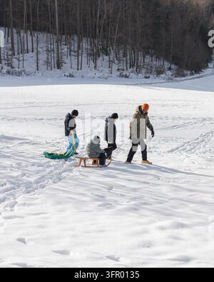 Vater und seine Söhne genießen eine verspielte Zeit im Schnee, lachen gemeinsam beim Schlittenfahren während eines unbeschwerten Winter-Familientages. Stockfoto