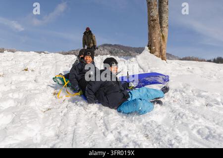 Glückliche Kinder genießen ein Schlittenabenteuer mit ihrem Vater, lachen und haben gemeinsam Spaß während eines unbeschwerten Familientages im Schnee. Stockfoto