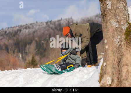 Kind genießt Schlittenfahren mit seinem Vater auf einem schneebedeckten Hügel, verbringt Qualitätszeit mit der Familie und genießt unbeschwerten Wintersport. Stockfoto