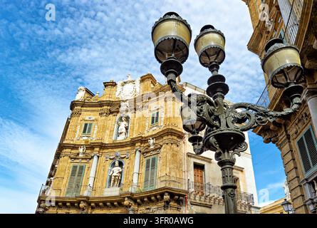 Niedrig angefertigte Aufnahme eines geschwungenen Eckgebäudes an der Piazza Vigliena, Sizilien, mit Statuen in Nischen und einem verzierten gusseisernen Laternenpfahl vor einem blauen Himmel Stockfoto