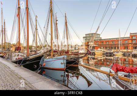 Historische Museumsschiffe, die im Hafen von Lübeck, Deutschland, vor Anker liegen, mit traditionellen Segelschiffen, hohen Masten und Ufergebäuden, die sich im ruhigen Wasser spiegeln Stockfoto