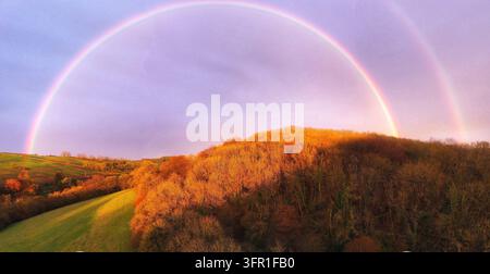 Luftpanorama eines doppelten Regenbogens über winterbraunem Waldland, orange vom Sonnenuntergang beleuchtet, Mendip Hills, Somerset, März 2023 Stockfoto