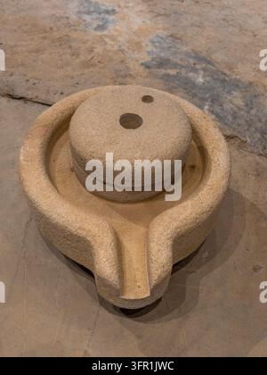 Traditionelle handgeschnitzte Steinquern-Rotationsmühle mit Ausguss zum Mahlen von Getreide, ausgestellt in einer Museumsumgebung. Stockfoto