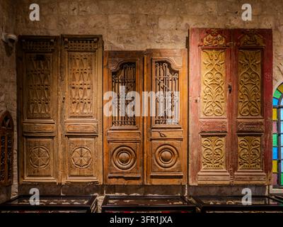 Sammlung von drei unterschiedlichen antiken hölzernen arabischen Türen mit aufwendigen Schnitzereien, Eisengittern und rot bemalten Details vor einer Steinmauer. Stockfoto