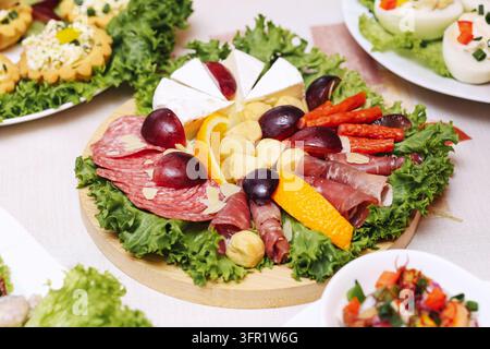 Dekorativer Aufschnittteller mit Salami, Käse, Weintrauben und frischem Gemüse. Party-Hintergrund für Catering, Vorspeisen und festliches Buffet. Stockfoto