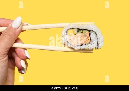 Lachs-Sushi-Rolle mit Holz-Chopsticks auf gelbem Hintergrund. Japanisches Essen Closeup für Mittagessen zum Mitnehmen, Meeresfrüchte und asiatische Küche. Stockfoto