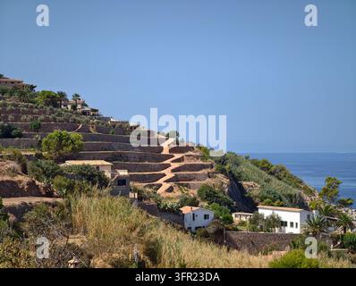 Ein weitläufiger Blick auf terrassierte Felder, die sich einen Hügel hinunter in Banyalbufar, Mallorca, Spanien, erstrecken und zum Mittelmeer führen. Traditionelle s Stockfoto