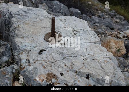 Alte rostige Bewehrungsstange, die in einem verwitterten Kalksteinblock im Freien eingebettet ist Stockfoto