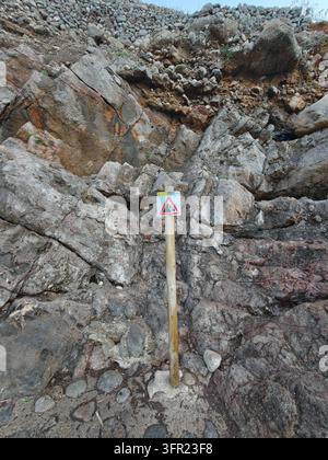 Eine Nahaufnahme eines Warnschilds "fallende Felsen", das deutlich auf einem Holzpfosten vor dem Hintergrund von rauen, strukturierten Felsformationen angebracht ist. Th Stockfoto