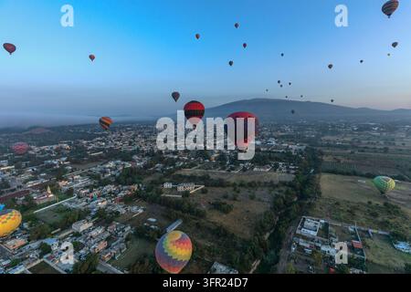 Dutzende farbenfroher Heißluftballons schweben bei Sonnenaufgang mit niedrigem Nebel über den Dächern von San Martin de las Piramides im Tal von Teotihuacan, Mexiko Stockfoto