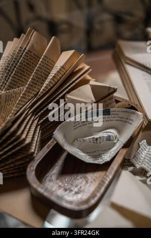 Eine Nahaufnahme von aufgefächerten alten Buchseiten, die einen strukturierten Hintergrund bilden. Ein kleines Papierboot, das aus zerrissenen Buchseiten gefertigt wurde, ruht in einem rustikalen Holz Stockfoto