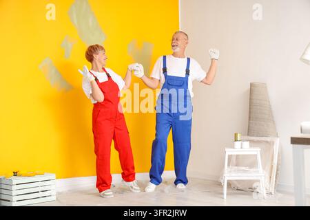Heimrenovierung und DIY-Projekt, glückliches Seniorenehepaar in Arbeitsanzügen malt Wände in einem neuen Haus während der Innenrenovierung und Hausreparatur Stockfoto