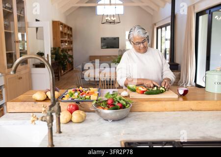 Senior Afroamerikanerin schneidet Gemüse in der Bauernhausküche auf einem Holzschneidebrett Stockfoto