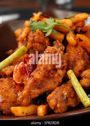 Nahaufnahme von trocken gebratenen Hühnerflügeln und Kartoffelstreifen mit Knoblauchsprossen und getrocknetem Chili Stockfoto