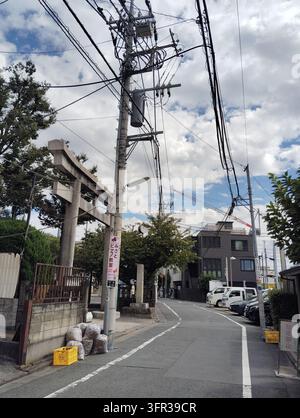 Eingang eines Shinto-Schreins mit Torii-Tor, Strommasten, Überheadkabeln und Müllsäcken in einer Wohnstraße in Tokio, Japan. Stockfoto