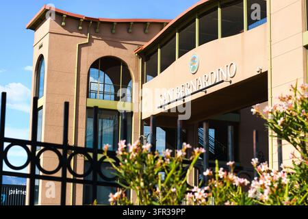 Eine braune Fußgängerbrücke der Station zeigt große Schriftzüge "San Bernardino" über einem schattigen Durchgang, eingerahmt von gebogenen Fenstern, einem schwarzen Zaun und rosa f Stockfoto