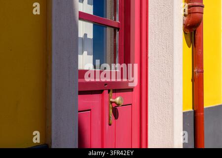 Eine rote Tür und ein passendes Fenster sind in eine gelbe Wand mit einem Metallabflussrohr gesetzt. Die kräftigen Farben schaffen eine grafische urbane Komposition in Coimbra. Stockfoto
