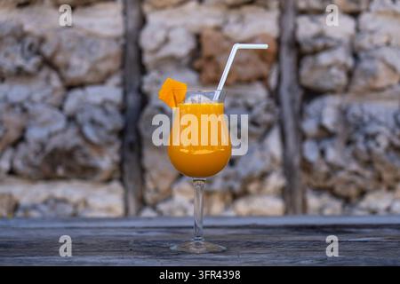 Frisch gepresster Mangohaft mit Mangoblatt in einem Glasbecher auf dem Hintergrund einer alten Steinmauer. Insel Sansibar, Tansania, Ostafrika. Clo Stockfoto