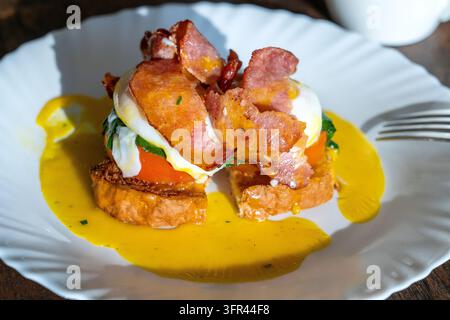 Eggs Benedict mit Speck, Toastbrot und Tomaten, Nahaufnahme. Sandwich mit pochiertem Ei zum warmen Frühstück Stockfoto