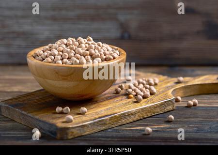 Getrocknete Kichererbsen in einer Schüssel auf einem Holzhintergrund. Verschüttete Kichererbsen. Selektiver Fokus Stockfoto