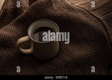 Kaffeetasse mit heißem dunklem Kaffee, der auf einem kuscheligen braunen Strickpullover entspannt und Wärme und Komfort bringt Stockfoto