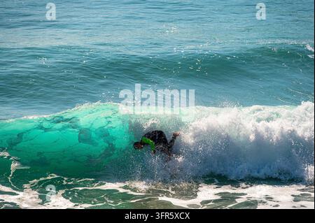 Surfer, der in einer brechenden türkisfarbenen Welle im Atlantik nahe der Küste von Andalusien, Spanien, an einem sonnigen Tag stürzt. Weißer Seeschaum und Wasser sprühen Stockfoto