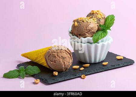 Vase und eine Waffeltüte mit hausgemachtem Schokoladeneis, bestreut mit Erdnüssen, serviert mit einem Minzgezweig auf pinkem Hintergrund, selektive Schärfe Stockfoto