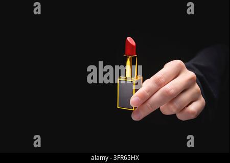Roter Lippenstift in der Hand einer Frau auf einem dunklen Hintergrund. Mädchen hält ein beliebtes Kosmetikprodukt Stockfoto