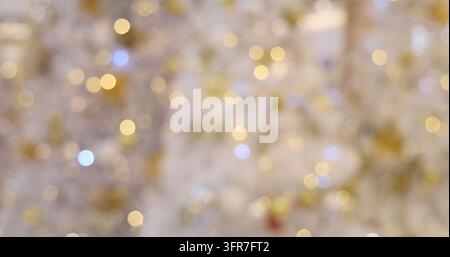 Bokeh-Lichter, die in einer festlichen Feiertagsumgebung glühen, warme goldene und weiße schimmernde Kreise, unscharfer dekorativer Hintergrund für saisonale Feierlichkeiten Stockfoto